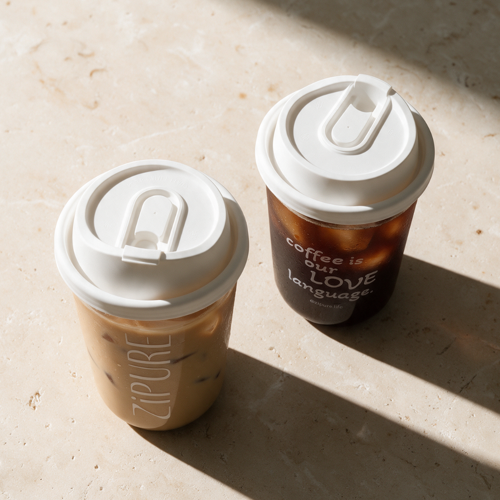 Two ZIPURE Grab & Sip 16oz iced coffee cups flat lay with white sip lids on stone surface