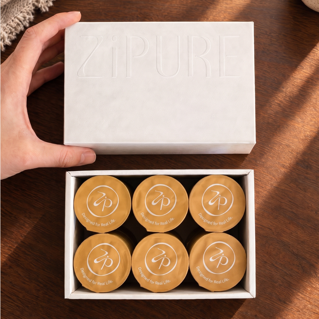 Hand opening a ZIPURE Never Lost in Milk box revealing six coffee pods